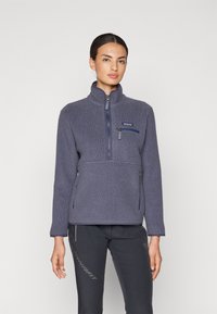 Felpa in pile di colore blu scuro con colletto alto, chiusura frontale a metà zip e due tasche laterali con zip; tessuto morbido e testurizzato.