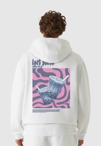 Hvit hettegenser med et trykt design som viser to drikkekopper på en rosa og lilla bølgete bakgrunn, tekst "lost youth coffee to go".