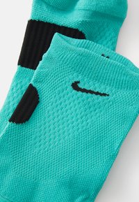 Sosete sportive turcoaz, fabricate dintr-un material texturat, prezintă accente negre și un logo negru. Designul include secțiuni cu nervuri pentru suport.