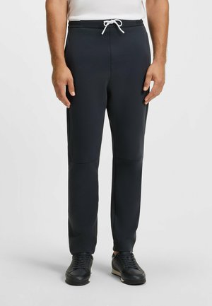 Navy jogger pants made of stretchy fabric with a drawstring waist, featuring a slim fit and side seam pockets. Paired with black sneakers.