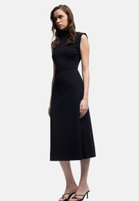 Vestido negro sin mangas con un escote alto, corte entallado y longitud midi fluida, confeccionado en una tela suave y elástica.