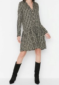 Svart blommönstrad klänning med långa ärmar, knäppning fram och en utsvängd kjol. Tillverkad av lätt tyg, i kombination med svarta knähöga stövlar.