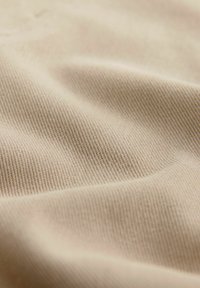 Beiger Stoff mit einer weichen Textur, der ein feines Rippmuster und sanfte Falten aufweist, was auf Flexibilität und Drapierung hinweist.
