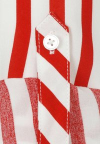Tissu rouge et blanc rayé avec un rabat boutonné, comprenant une partie de col arrondi et des détails de couture. Apparence texturée avec des couleurs contrastées.