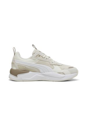 Beige og hvide sneakers med en struktureret overflade, en distinkt sålform og en dekorativ gummidetalje på hælen. Subtil logo detalje inkluderet.