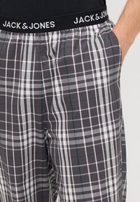 Hallid halli ja valge ruuduline puhkepüksid tumeda vöökohtaga, millel on "JACK & JONES" tekst; sisaldavad taskuid, on valmistatud puuvillast ja pakuvad mugavat istuvust.