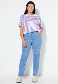 Lila och vit randig skjorta med ett hjärtapplikation, i kombination med ljusblå jeans med en hjärtbrodering på låret. Bärs med vita skinnskor med nitar.