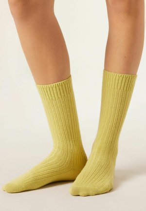 Gelbe gerippte Socken aus weichem Material, mit einer mittellangen Länge bis zur Wade und einer glatten Textur, die einen eng anliegenden Bund und einen verstärkten Zehenbereich aufweisen.