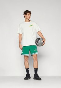 Wit Nike T-shirt met korte mouwen en een meerkleurig logo, gecombineerd met groene basketbalshorts met witte accenten en logo, zwarte basketschoenen.