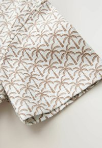 Bomullstyg med ett upprepande mönster av palmträd i brunt på en ljusbeige bakgrund. Kortärmad design med vikta fållar.