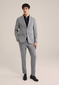 Grijs geblokt pak met een enkelgeknoopte blazer, gecombineerd met een marineblauw poloshirt en zwarte nette schoenen. Glad stof, op maat gemaakte pasvorm.