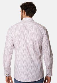Camisa blanca de manga larga con un sutil patrón de hojas repetido en marrón claro. Presenta un collar clásico y puños con botones. Textura de tela suave.