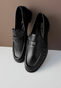Musta nahkainen loaferit, joissa on sileä pinta, pyöristetty kärki, koristeellisia ompeluja ja matala korko. Hienovarainen brändilogo näkyy sisällä.