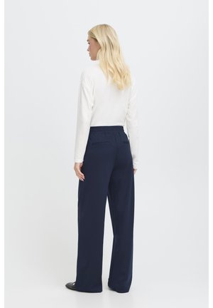 Pantalons larges bleu marine avec une taille élastique, associés à un haut blanc à manches longues. Le tissu semble lisse avec un minimum de détails.