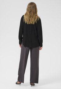 Zwarte langärmige shirt met knoopmanchetten, gecombineerd met losse grijze broek. Soepele stof met een relaxte pasvorm. Minimalistisch ontwerp.