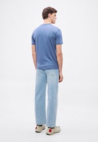 Světlomodré tričko s krátkým rukávem, volný střih, bavlněný materiál. Kombinováno s džíny se světlým vypráním a rovnými nohavicemi a béžovými teniskami s červenými akcenty.