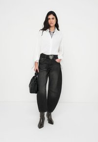 Λευκό πουκάμισο με φαρδιά μανίκια, γκρι καρό γιακάς, συνδυασμένο με ψηλόμεσα μαύρα τζιν, ζώνη με καρδιά ως πόρπη και μαύρη τσάντα.