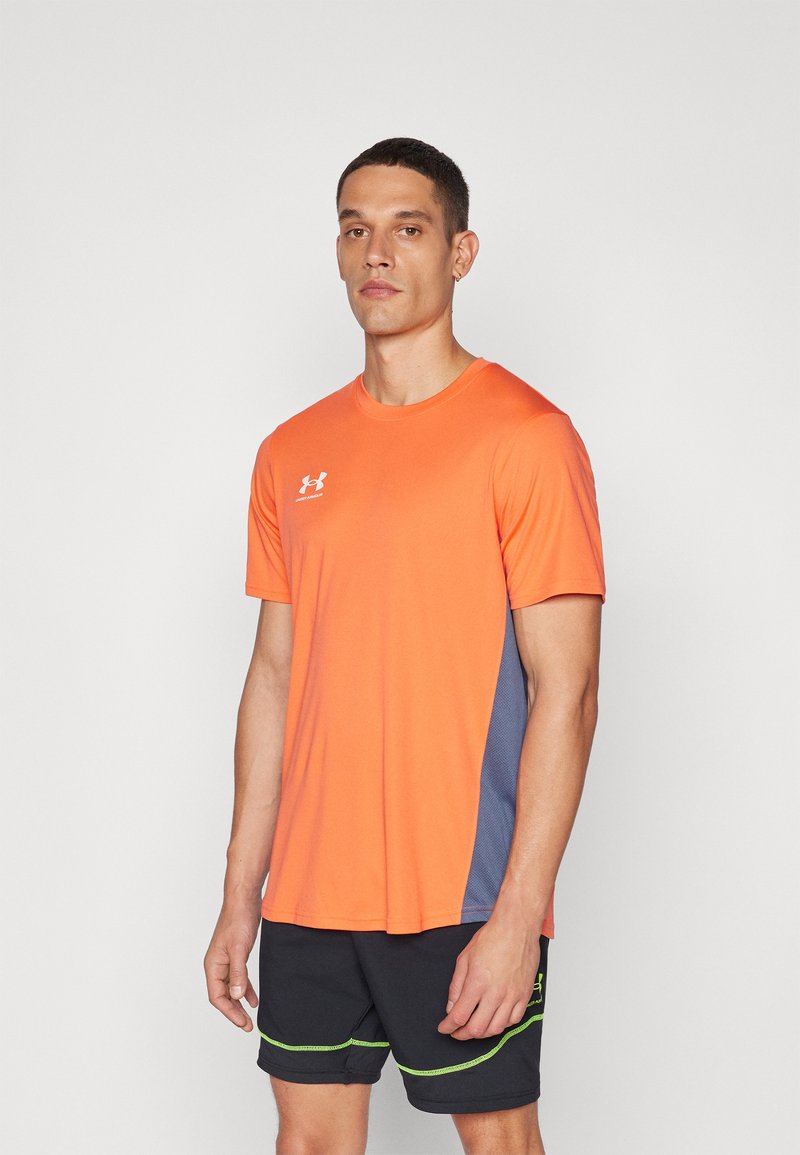 Oransje treningst-skjorte med korte ermer, med en marineblå sidepanel og Under Armour-logo. Stoffet ser ut til å være pustende og lett.