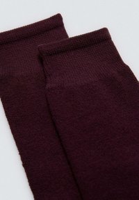 Calcetines tobilleros burdeos hechos de una suave tela de punto con una textura lisa. Presentan puños acanalados. Diseño sencillo sin patrones ni acentos.