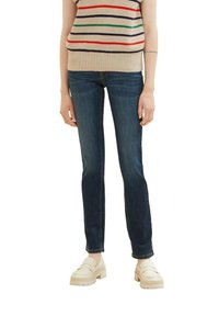 Jean en denim foncé avec une coupe slim et des coutures discrètes. Associé à un haut en tricot beige à rayures multicolores et des chaussures à plateforme de couleur claire.