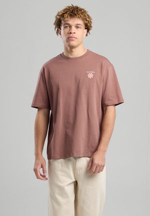 Camiseta de manga corta marrón en suave tejido de algodón. Presenta un pequeño gráfico floral y el texto "CALIFORNIA" en rosa claro en el pecho.