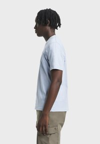 T-shirt di cotone azzurro chiaro a maniche corte indossata da una persona, con collo rotondo e taglio dritto, abbinata a pantaloni cargo verde oliva chiaro.