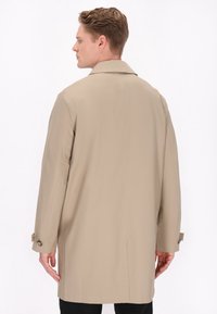 Beige trenchcoat med klassisk krave, lange ærmer og knaplukning ved ærmerne. Har glat stof og lige snit design.