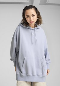 Hoodie surdimensionné bleu clair avec une poche kangourou, une capuche à cordon de serrage et des poignets côtelés, arborant un petit logo sur la poitrine.