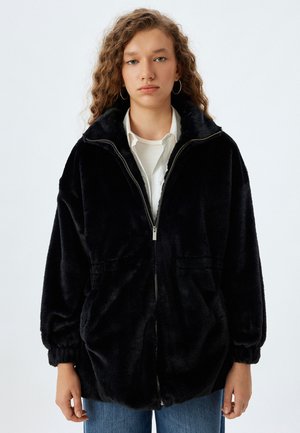 Veste en polaire noire avec fermeture éclair à l'avant, poignets côtelés et deux poches avant ; texture douce avec un design à coupe décontractée.