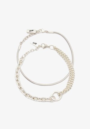 Kaksi toisiinsa kietoutunutta hopeaketjubraceletia, joissa on hummeriankkurit ja pienet suorakulmaiset tarrat, joihin on kaiverrettu allekirjoitus.