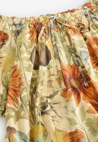 Tissu épaules dénudées avec encolure élastique et imprimé floral aux tons orange, jaune, vert et crème, noué avec un fin cordon en nœud.
