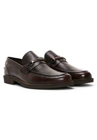 Bruine leren loafers met een gestructureerde afwerking, voorzien van een decoratieve band en metalen accent, ronde neus en lage gestapelde hak.