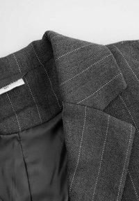 Szary, teksturowany żakiet w białe prążki, z satynową podszewką i klapami. Wewnętrzna tkanina jest gładka i ciemna.