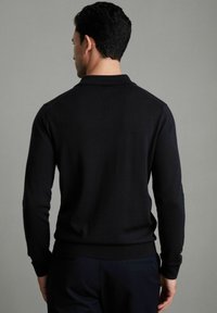 Pulover negru tricotat cu guler, mâneci lungi și manșete și tiv ribbelate. Textura pare netedă și ajustată.