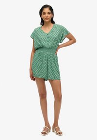 Jugar de manga corta verde con escote en V, cinturilla elástica y un patrón floral blanco en toda la prenda. Cuenta con un corte relajado y pantalones cortos.