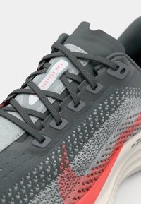 Baskets Nike Pegasus, avec un dessus en mesh gris, des accents rouges, des lacets gris plats, des œillets renforcés, des motifs texturés et une semelle rembourrée.