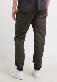 Olivově zelené joggingové kalhoty vyrobené z lehkého materiálu, s elastickými manžetami na kotnících a volným střihem.