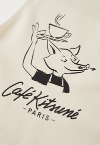 Kremfarget stoff med en svart illustrasjon av en rev som holder en kaffekopp på et brett, ledsaget av teksten "Café Kitsuné Paris."