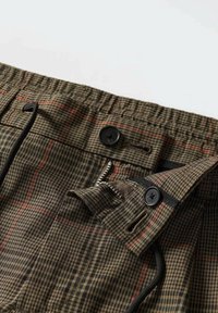 Brązowe szorty w kratę z elastycznym paskiem, czarnymi guzikami, sznurkiem do regulacji oraz zapinaną na zamek kieszenią z przodu, zapewniającą bezpieczne przechowywanie.