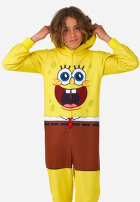 Pijama de una pieza amarillo de SpongeBob SquarePants con cierre de cremallera, que presenta grandes ojos azules, una boca sonriente, pantalones marrones y acentos de patrón verde.