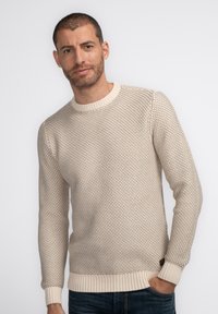 Light beige sweater with a textured knit pattern, round ribbed neckline, and ribbed cuffs and hem. Worn over dark blue jeans.
