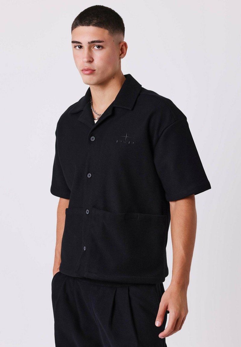 Camicia nera a maniche corte con bottoni e colletto, dotata di taschino frontale e dettaglio logo discreto. Tessuto textured e vestibilità rilassata.