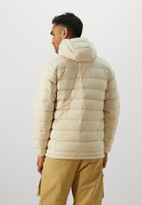 Beige puffer jacket with horizontal quilted pattern and hood. Smooth texture, lightweight design, layered stitching, and elastic cuffs.