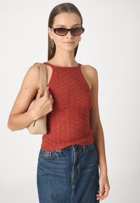 Débardeur en tricot rouge avec un motif en losange, doté d'un col haut et de fines bretelles, associé à une jupe en jean et un sac à main beige.