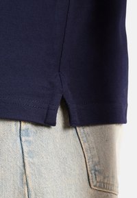 Camisa de manga corta azul marino con una tela texturizada, que presenta un detalle de abertura lateral. Combinada con jeans de mezclilla azul claro con un patrón desteñido.