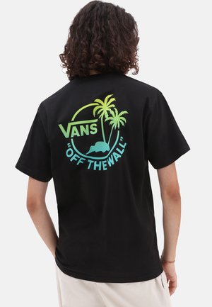 Personne aux cheveux bouclés portant un t-shirt Vans noir affichant un logo de palmier bleu et vert ainsi que le texte « Off The Wall » au dos.