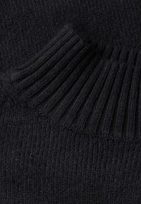 Gros plan d'un tissu tricoté noir montrant des motifs de couture côtelés et texturés.