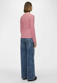 Röd och vit randig långärmad topp med rund halsringning, kombinerad med högmidjade, vida blå denimjeans.