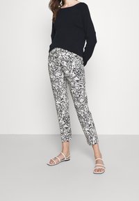 Zwarte gebreide trui, geprinte wit- en zwart gekleurde broek met bloemenpatroon, en witte sandalen met bandjes. De broek heeft een taps toelopende snit.