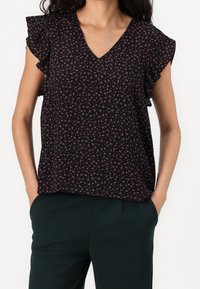 Blusa nera a maniche corte con scollatura a V, caratterizzata da un motivo floreale nei toni del rosa e del bianco, con accenti di maniche arricciate; il tessuto appare leggero.